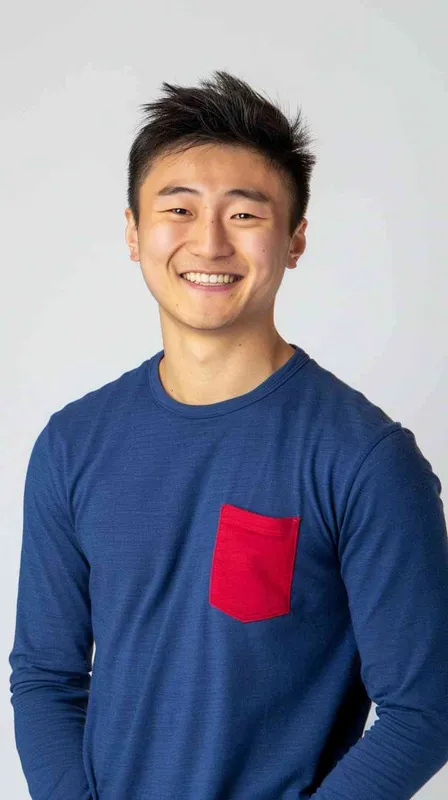 A young Chinese man with short black hair, wearing a blue long-sleeved shirt with a red pocket on the chest area of his right hand is smiling at the camera. The background color should be white to highlight his face. He has an Asian nose shape, medium skin tone, round eyes, and thin eyebrows. His overall appearance conveys friendliness or confidence. in the style of --ar 25:32 - style3部分