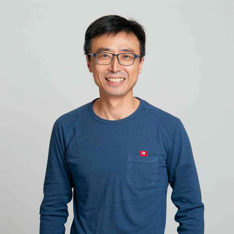 A Chinese man with black hair, wearing a blue long-sleeved shirt and red logo on the chest of Levis jeans is smiling at the camera in a front view. The background color should be white to highlight his facial features. He has short hair and wears glasses that reflect light, giving him a portrait style in the authentic style. His expression conveys confidence as he stands against a clean backdrop. High resolution, professional photograph, and detailed skin texture. Portrait photography. --ar 25:32 - style3部分