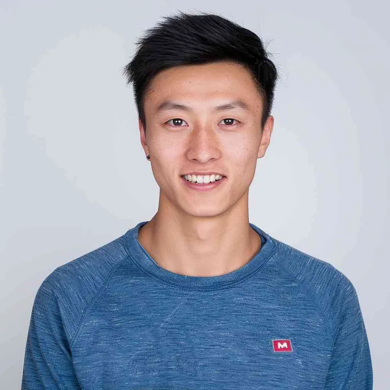 A Chinese man with black hair, wearing a blue long-sleeved shirt with a red logo on the chest is smiling at me from the front view. The background color should be white to highlight his facial features. He has short, dark brown eyes that sparkle slightly when he looks in my direction. His face shows confidence and vitality in the style of Levis. --ar 25:32 - style2部分