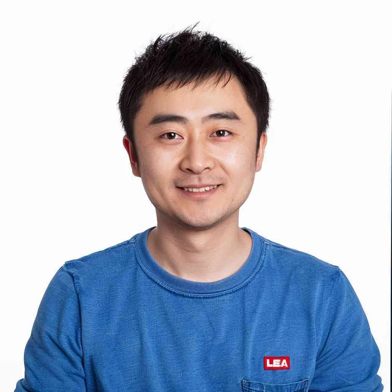 A Chinese man with black hair, wearing a blue long-sleeved shirt with a red logo on the chest is smiling at me from the front view. The background color should be white to highlight his facial features. He has short, dark brown eyes that sparkle slightly when he looks in my direction. His face shows confidence and vitality in the style of Levis. --ar 25:32 - style3部分