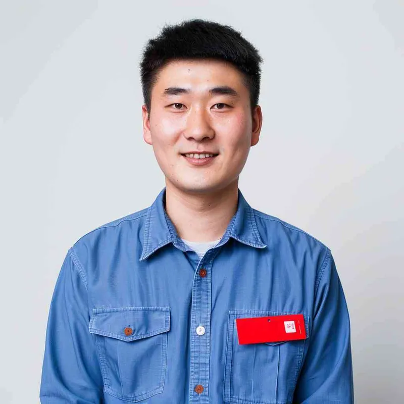 A young Chinese man with short black hair, wearing a blue long-sleeved buttoned shirt and a red name tag on his chest, smiling at the camera against a white background for a professional profile picture. The image is in the style of a typical company profile photo. --ar 25:32 - style2部分