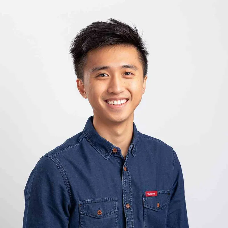 A young Chinese man with short black hair, wearing a blue long-sleeved buttoned shirt and a red name tag on his chest, smiling at the camera against a white background for a professional profile picture. The image is in the style of a typical company profile photo. --ar 25:32 - style4部分