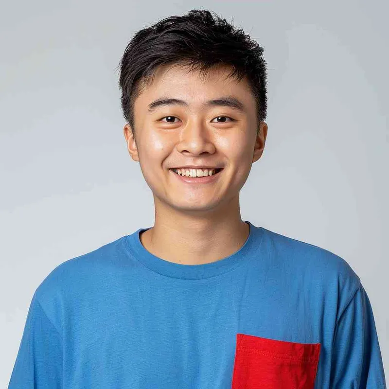 A young Chinese man with short black hair, wearing a blue long-sleeved shirt with a red pocket on the chest area of his right hand is smiling at the camera. The background color should be white to highlight his face. He has an Asian nose shape, medium skin tone, round eyes, and thin eyebrows. His overall appearance conveys friendliness or confidence. in the style of --ar 25:32 - style3部分