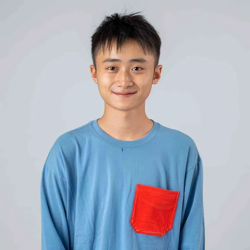 A young Chinese gril with short black hair, wearing a blue long-sleeved shirt with a red pocket on the chest area of his right hand is smiling at the camera. The background color should be white to highlight his face. He has an Asian nose shape, medium skin tone, round eyes, and thin eyebrows. His overall appearance conveys friendliness or confidence. --ar 1:1 --q 1 --v 6.0 - style1部分