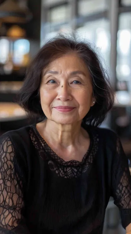 A middle-aged Asian woman with black hair, smiling and looking at the camera, wearing casual , is sitting in an office or restaurant. The background features natural light and bright colors, creating a warm atmosphere. She has exquisite facial details, full of vitality. The photography uses soft lighting, a medium shot composition, and captures her natural expression. The image has realistic skin texture and a cinematic effect with the best quality.  - style3部分