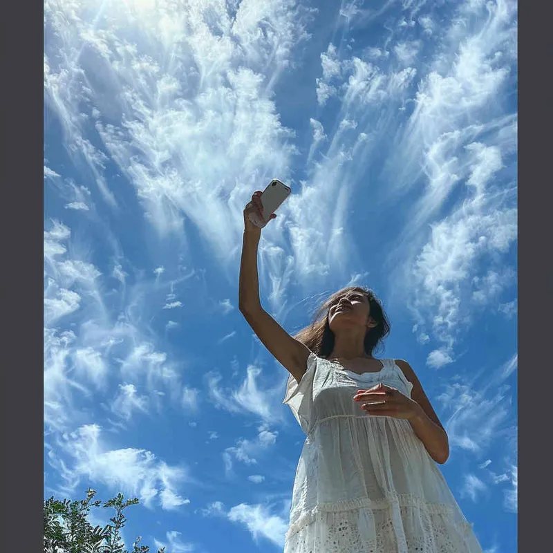 天空一下，一个女性背景拿着手机举过头顶拍照，一辆飞机里飞行员点赞的姿势看像镜头，星海成风格，蓝天白云绿树 - style2部分
