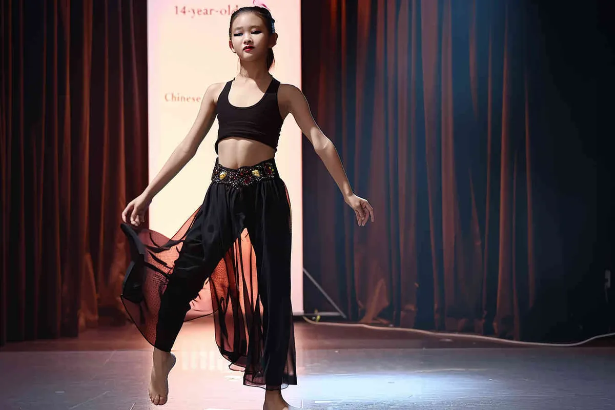 A 14-year-old Chinese girl, elegantly adorned in a jazz suit, dances with grace on a grand stage, with spot light, face directly into the front. As she captivates the audience, every flawless movement is beautifully captured through the lens of a Canon 85mm f1.2 camera, high quality, high res, 8k, raw, photo reliastic -no text - style3部分